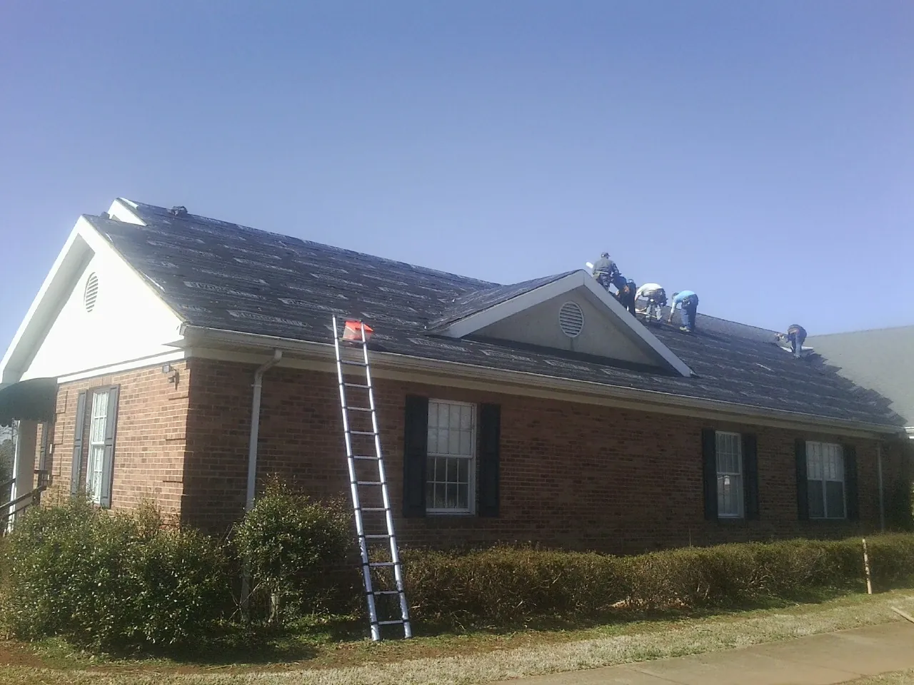 Crew tearing shingles off a brick ranch roof with a ladder set — Emergency Roof Repair work by our crew in Sandy Hook