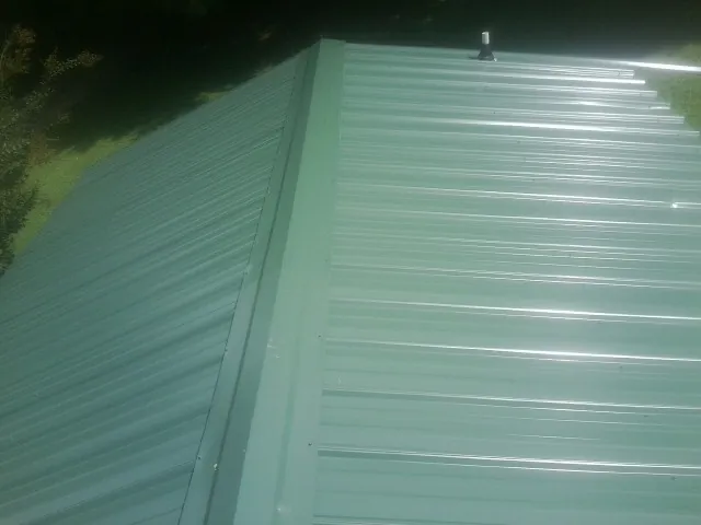 New green metal panels meeting at the ridge of a roof — Flat Roof Repair work by our crew in Sandy Hook